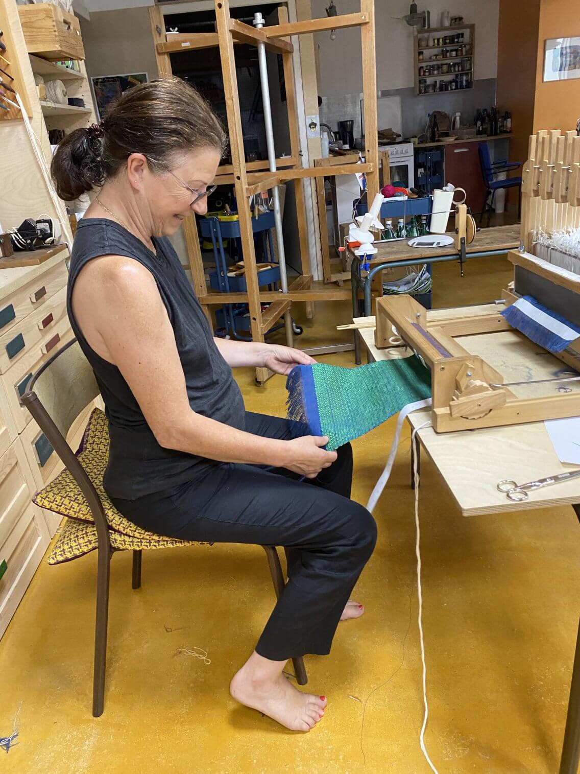 Une élève observe le résultat de son tissage, il fait chaud, on tisse pieds nus !