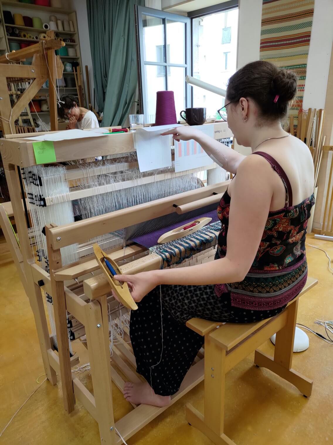 Elève en cours de tissage se référant à son modèle.
